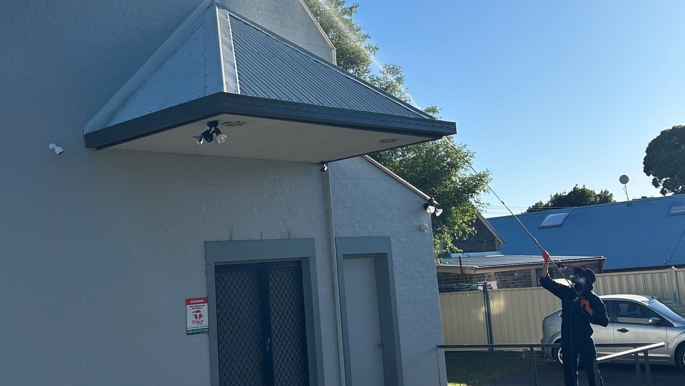 A BFYB technician spraying the eaves of a commercial building with an extension lance