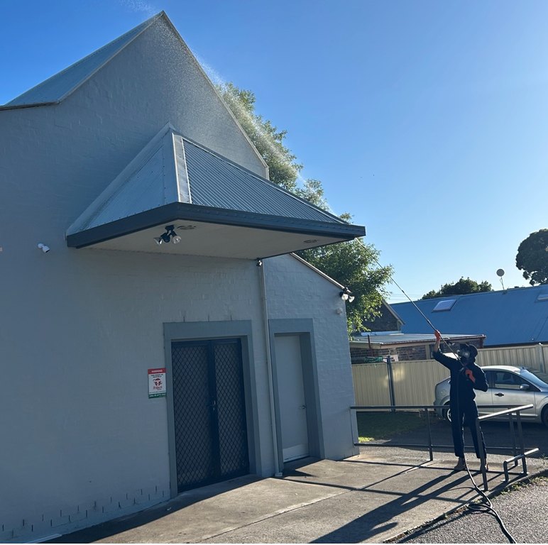 A BFYB technician spraying the apex of a two-storey gable with a telescopic wand, standing on the ground